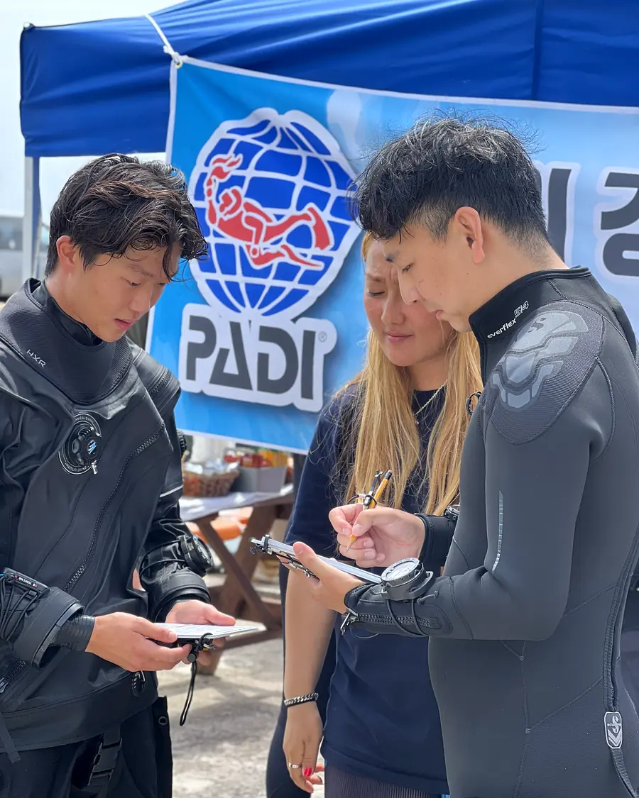 PADI 텐트 앞에서 슬레이트로 평가 내용을 확인하는 후보생과 평가관